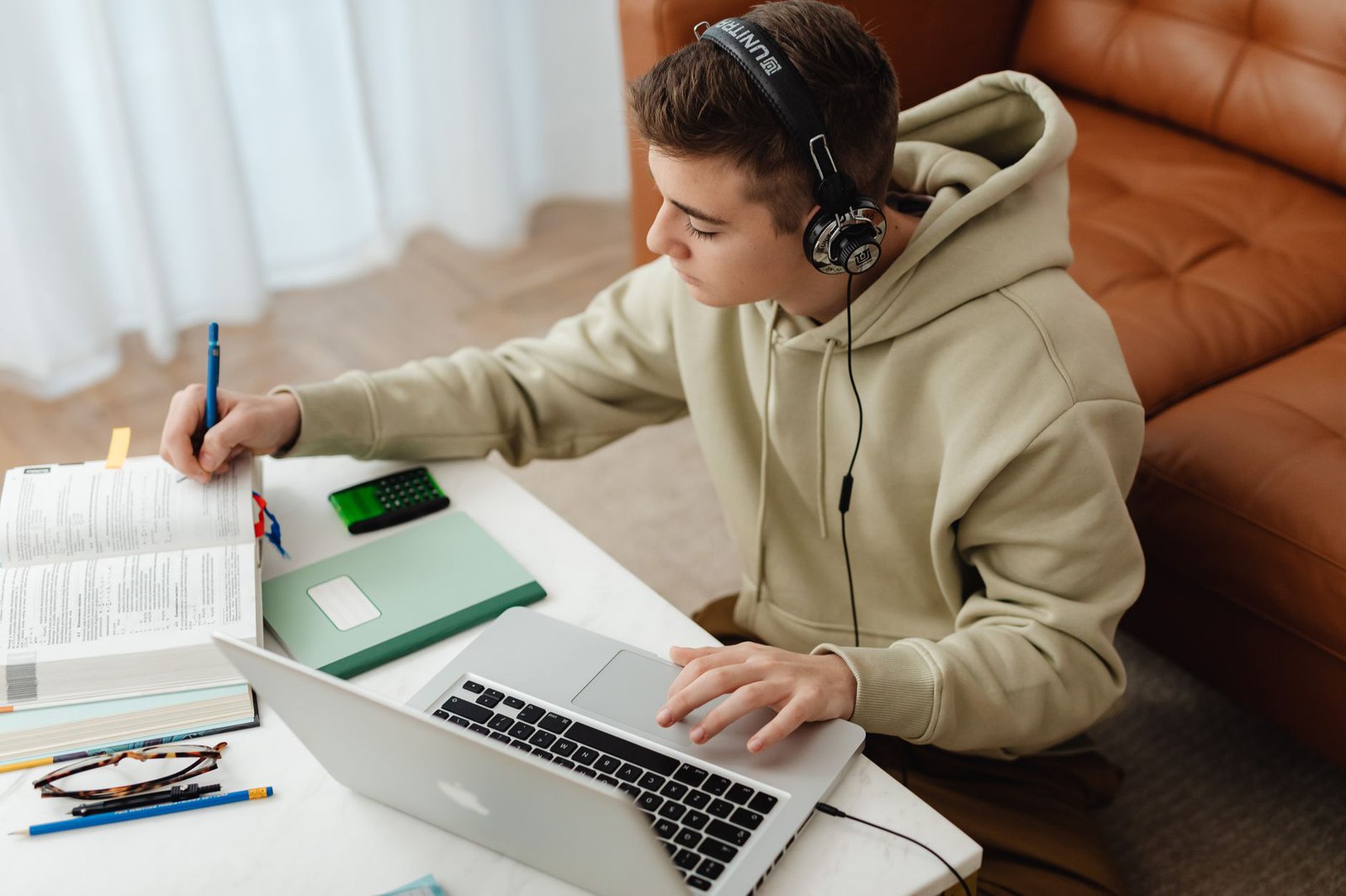 Student wearing headphones studying at a laptop with a textbook, notebook and calculator
