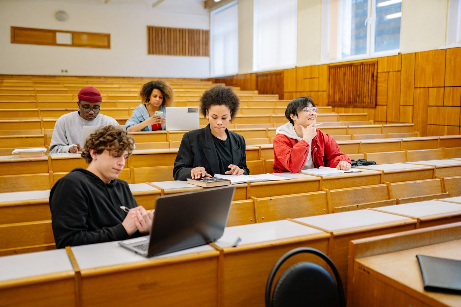 Students using a laptop and study notes in a university lecture hall, illustrating the study setting for Recallify AT software